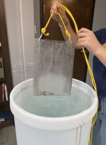 A wire container with hearing aids is lowered into a bucket of water to test the waterproof claims of various hearing aids