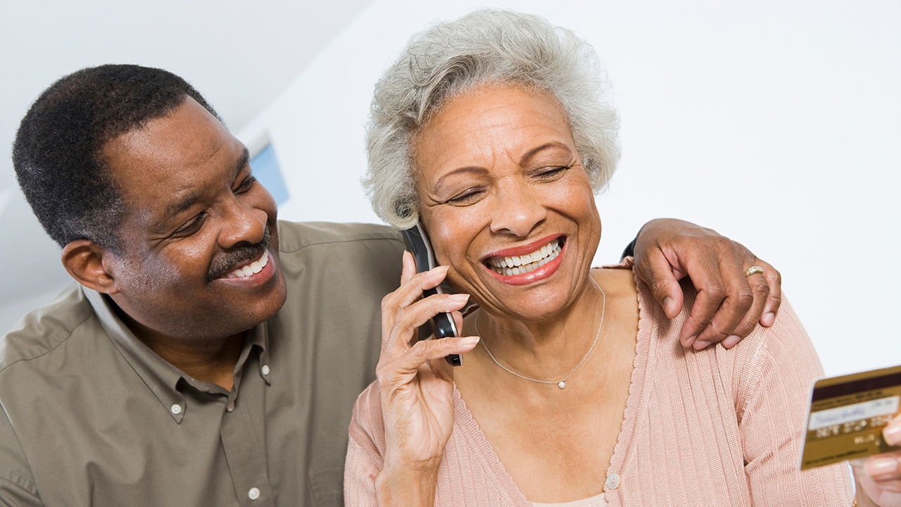 Happy senior African American woman on call while holding credit card with man besides her