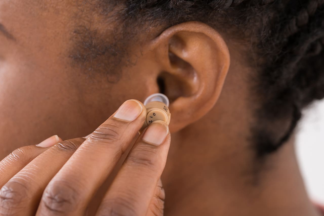 Close-up Of Female Hand Putting Hearing Aid In Ear