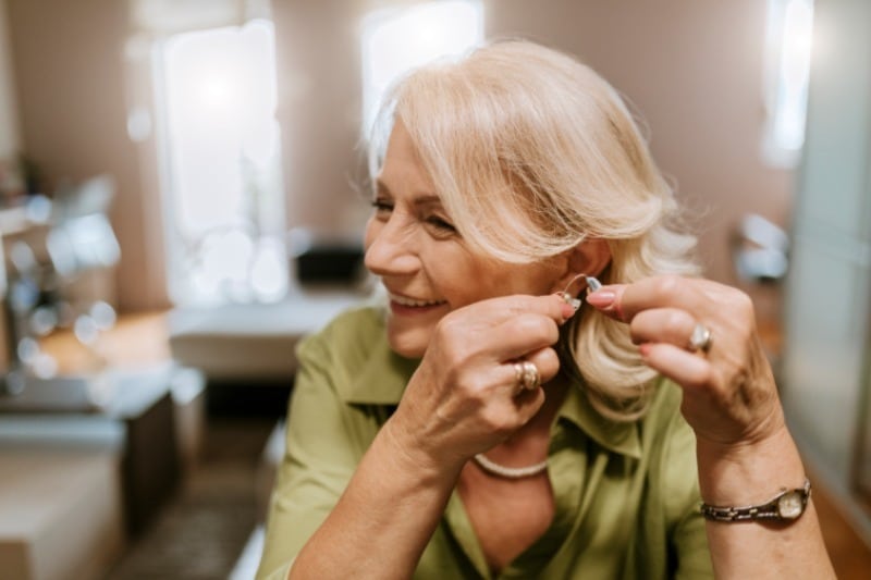 Senior woman smiles while applying a hearing aid in her ear