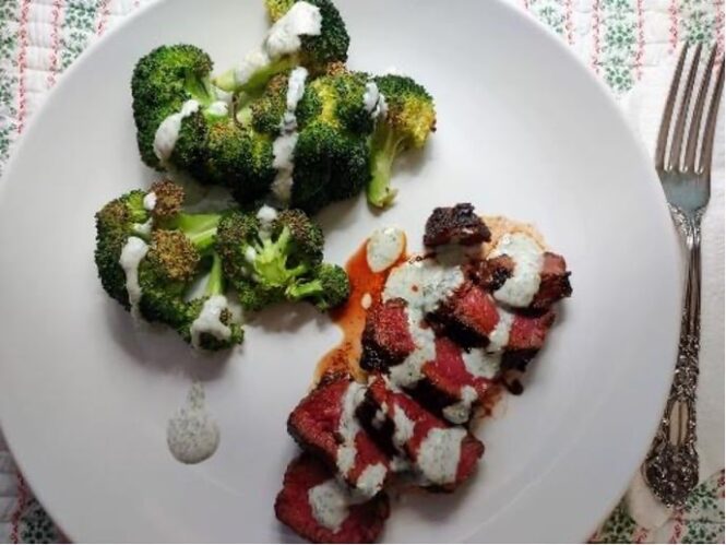 delicious cooked steak on a white plate with a side of broccoli and drizzle of creamy sauce
