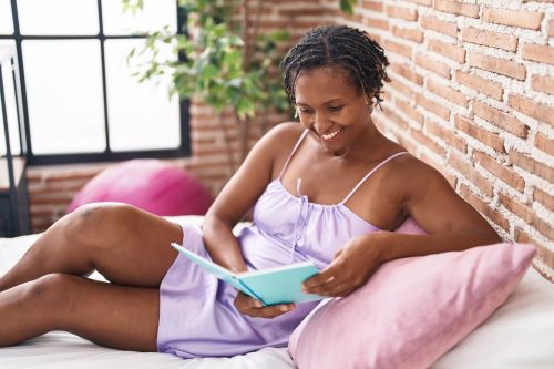 Woman reclining on bed at home with book