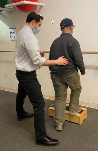 A physical therapist helping a patient perform step ups to improve stair climbing skill.