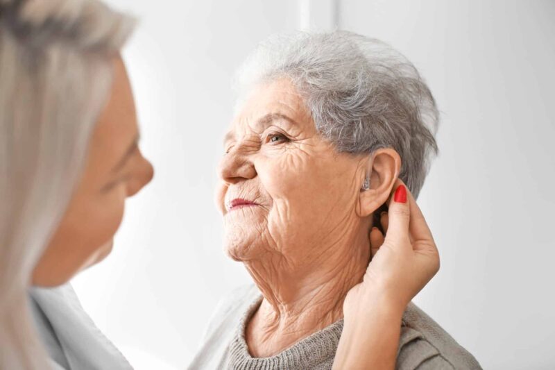 Woman fitting older adult with hearing aid