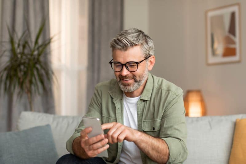 Older adult man wearing glasses using smartphone at home