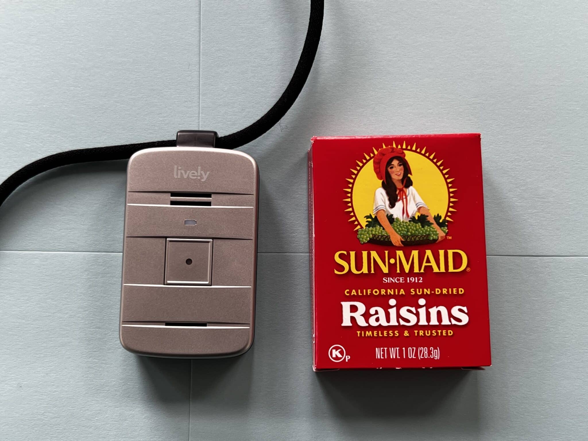 Lively Mobile Plus medical alert system size compared to box of raisins on a blue background