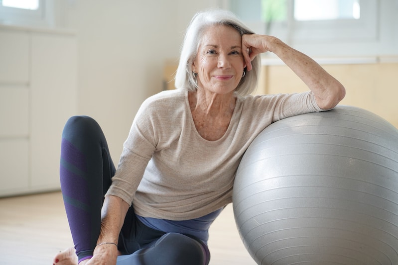 Older woman sitting on floor leaning against exercise ball