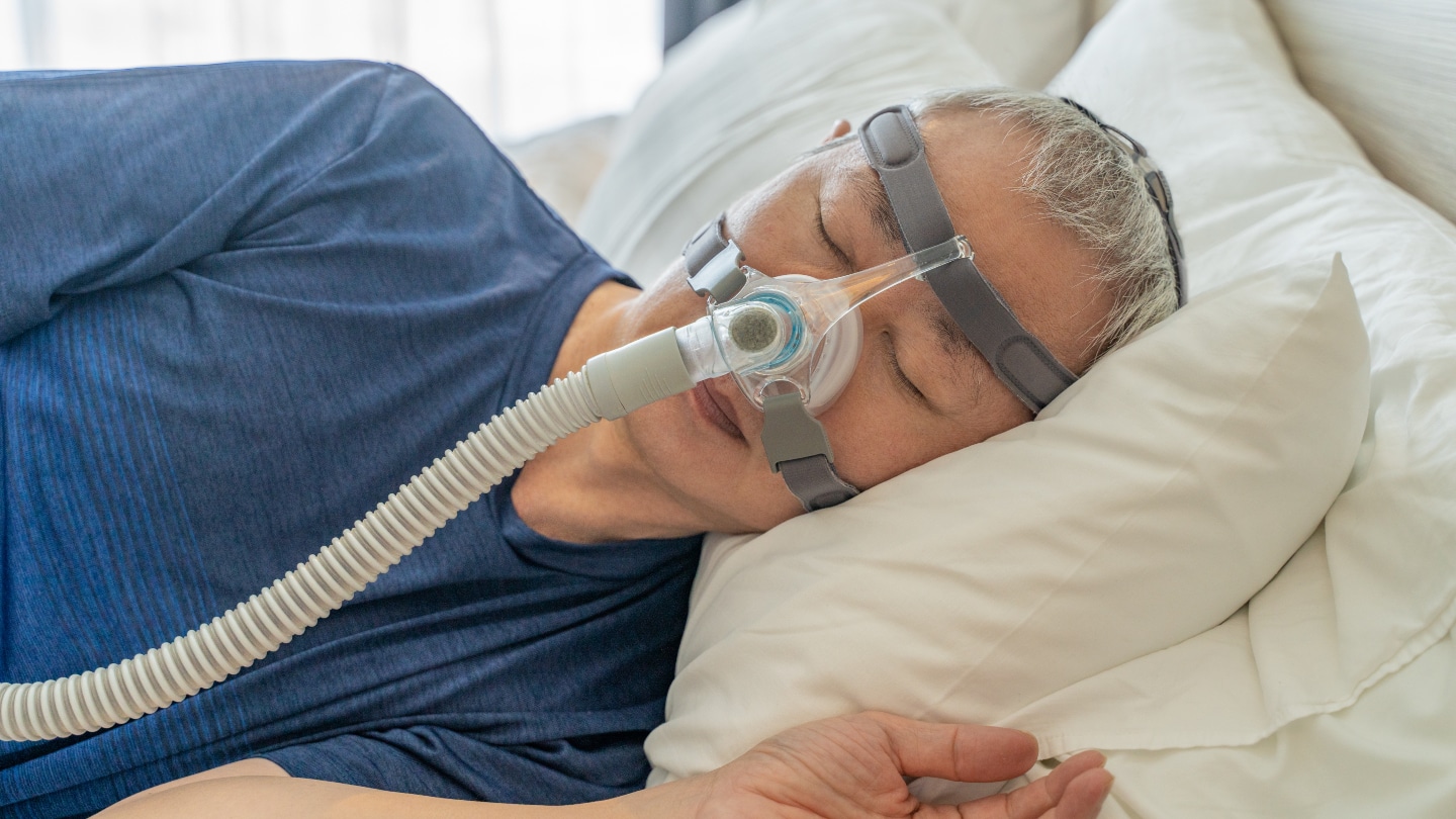 Middle age man wearing CPAP mask and headgear to help with his sleep apnea while sleeping in his bed in his bedroom