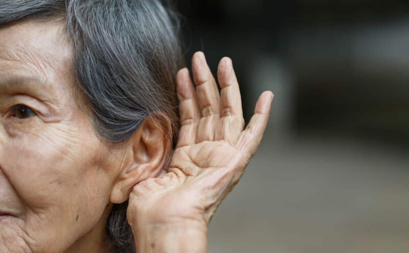 Older adult with their hand cupped around their ear hearing