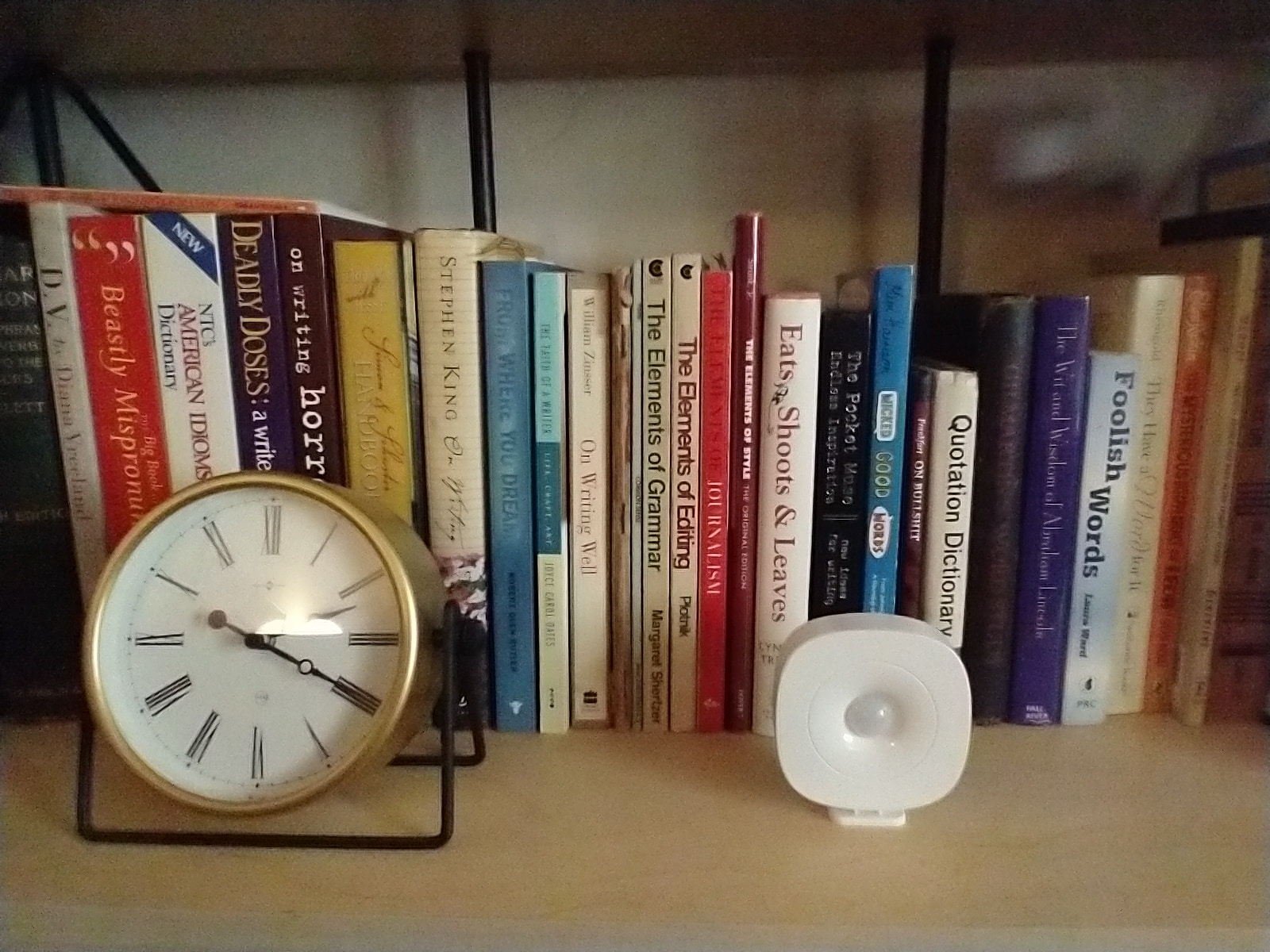 Aloe Care Health motion sensor on a bookshelf next to a clock.