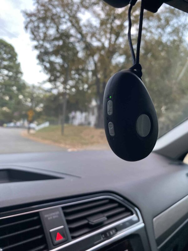Mobile medical alert system hanging from a car rearview mirror.