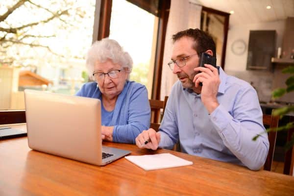 Older woman and younger man looking at laptop screen while the man is on the phone