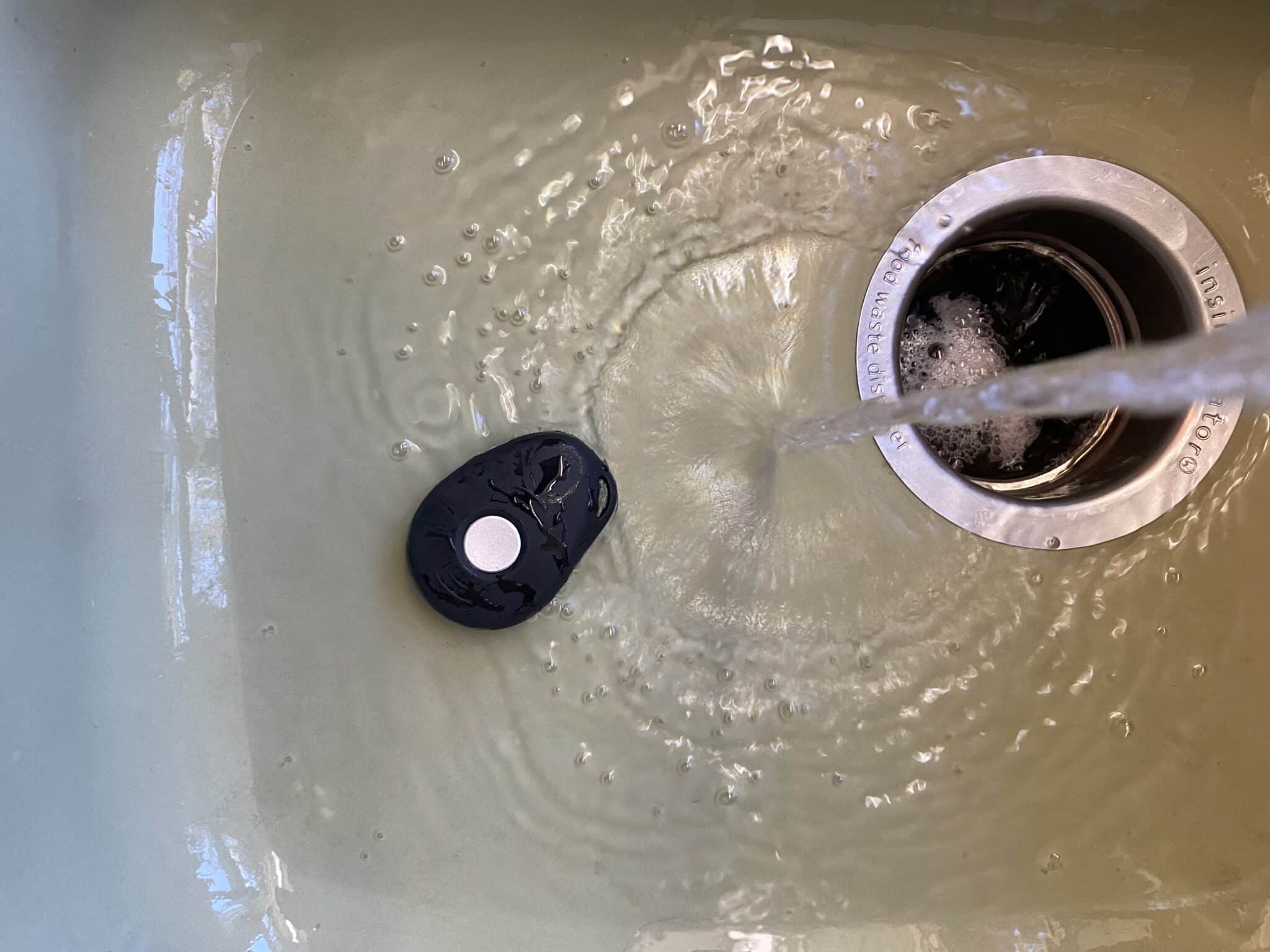 Black LifeFone mobile medical alert system in a sink with running water splashing on it