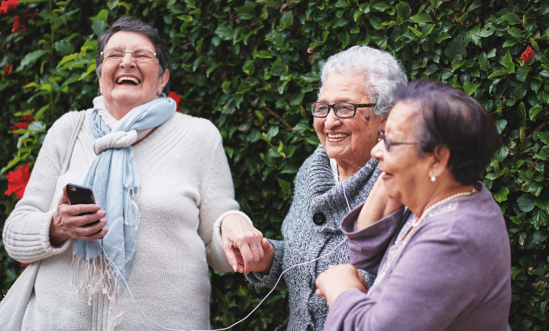 Three older women laughing and listening to music with earbuds on a cellphone