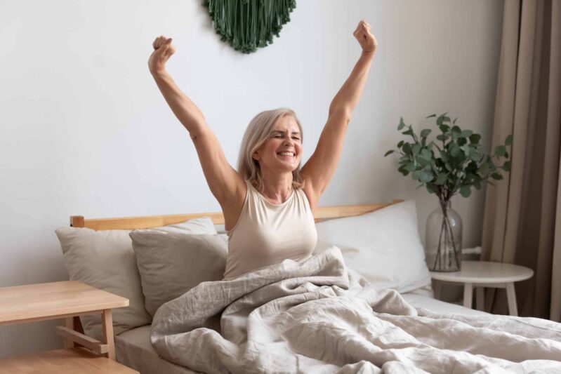 Older adult sitting up in bed stretching
