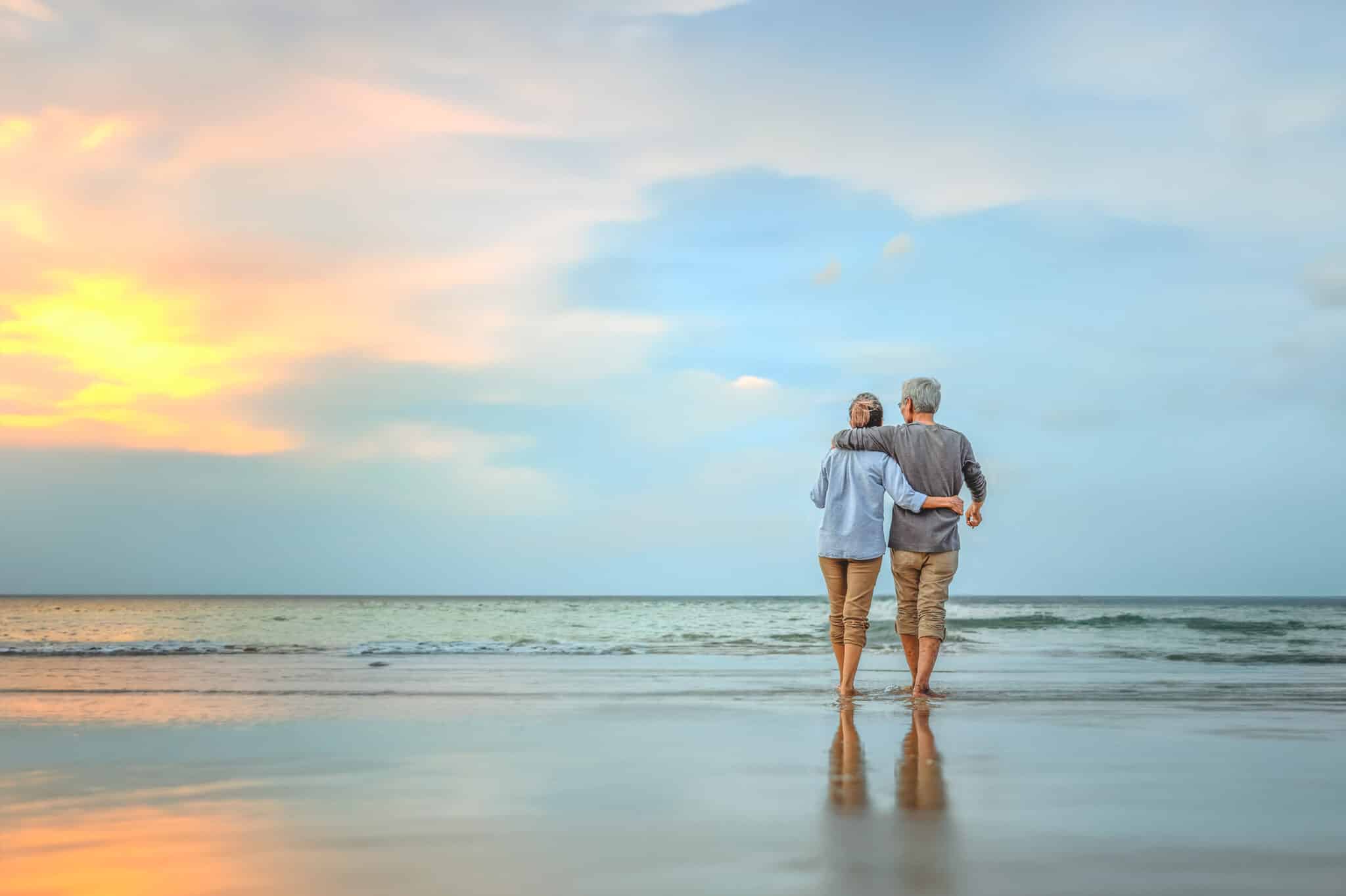 Senior couple walking on the beach holding hands at beach sunrise in evening.