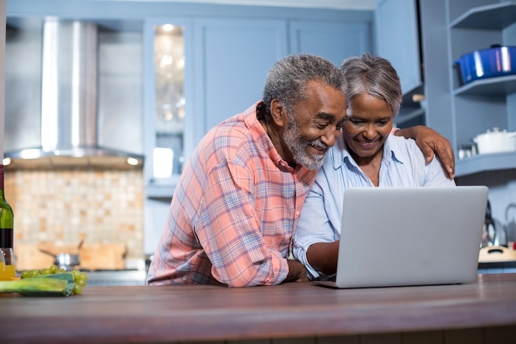 An older man and woman using a laptop at a kitchen counter