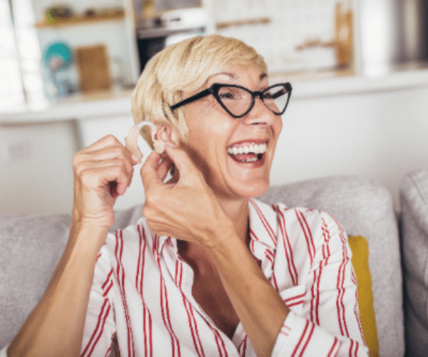 Woman smiling and putting behind-the-ear hearing aids in place