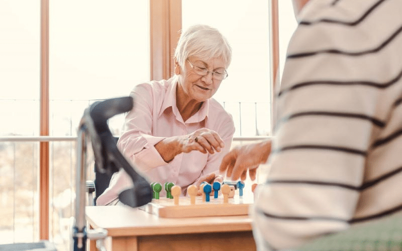 Two older adults playing a board game in a sunny room.