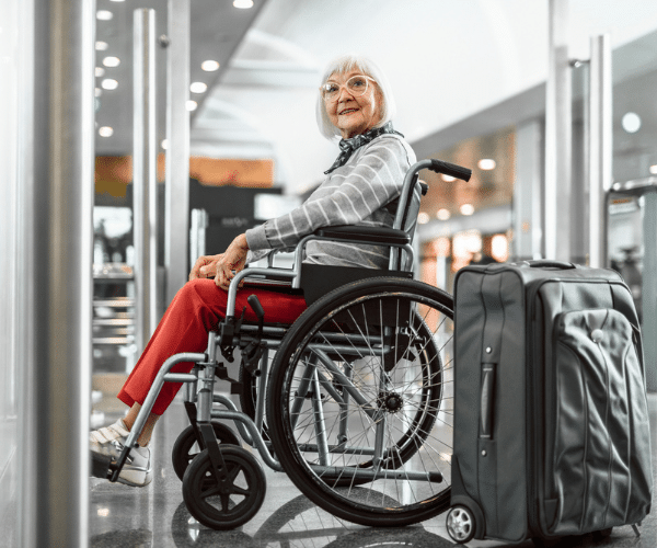 Happy older woman in wheelchair with a suitcase at airport