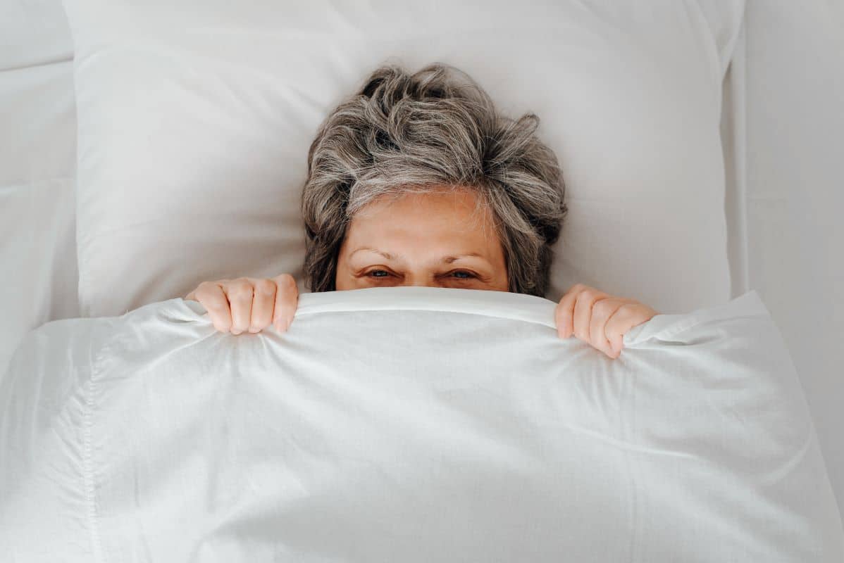 Person playfully sleeping in bed with white sheets