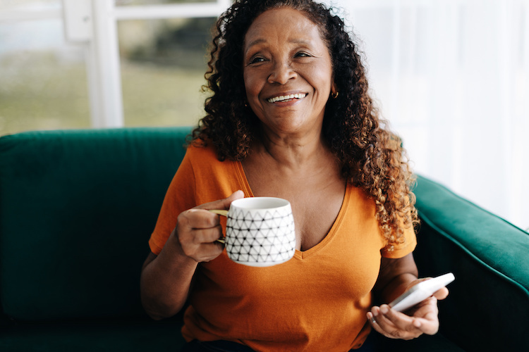 Woman on her cellphone smiling and holding a cup of coffee