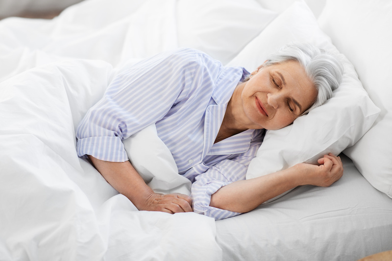 Older woman happily asleep in bed | CAPTION: Cooling mattresses help you get a restful night’s sleep