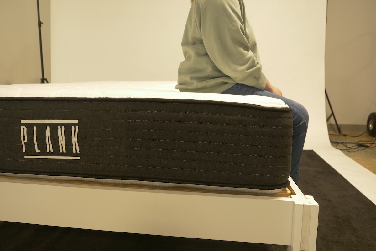Woman sits on the edge of a Plank mattress to test edge support