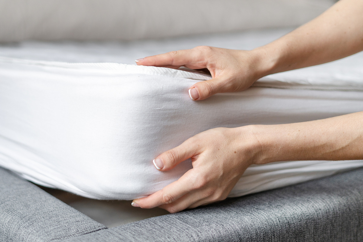 Two hands putting a white sheet onto a mattress.